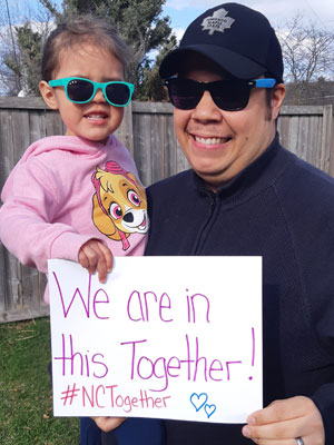 Man holding young girl with sign that reads: We are in this together!! #NCtogether