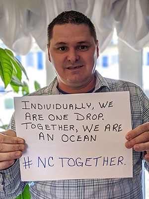Man holding a sign reading: Individually, we are one drop. Together, we are an ocean. #nctogether