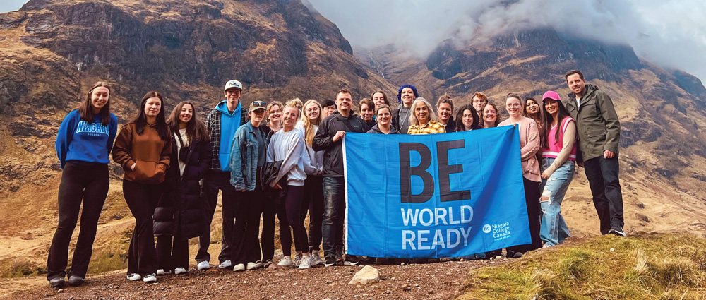 Group of staff and students holding a Be World Ready flag with the stunning backdrop of misty mountains