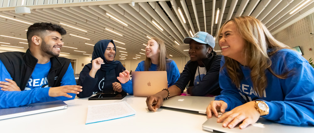A group of 5 diverse students studying together with their laptops around a table