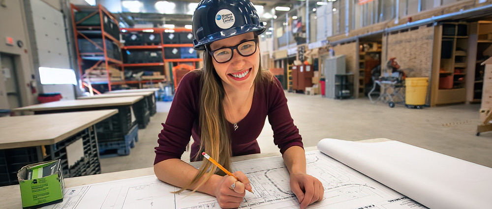 Smiling female student wearing NC hard hat works on CAD drawings with a pencil